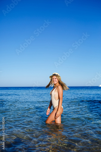 Sexy, cheerful, light, cheerful, fair-haired girl in a hat, in a beige swimsuit. Sandy beach, cliffs, vacation at sea.