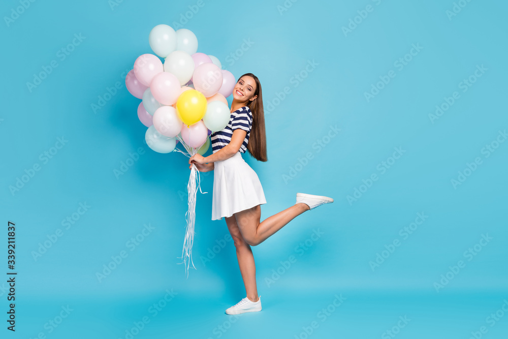 Full length profile photo of beautiful pretty lady good mood bring many air balloons friend birthday event wear striped t-shirt white short skirt footwear isolated blue color background - obrazy, fototapety, plakaty 