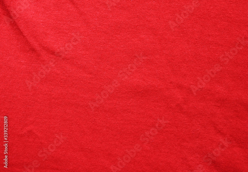 Red fabric texture background with wrinkles. Worn red clothing structure, creased pattern element, casual stylish cotton shirt background close up top view