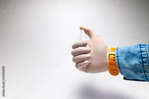 A male hand in a rubber white glove and a denim shirt holds applying a sanitizer spray against viruses. Concept for the successful use of antiviral agents during a pandemic
