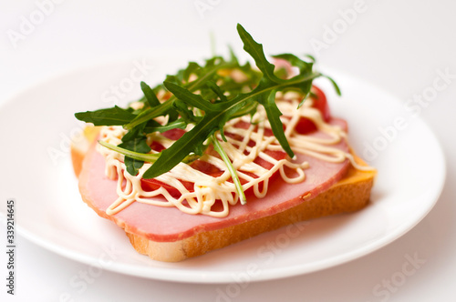 Sandwich of bread for toast, sturgeon, tomatoes, arugula, cheese and mayonnaise on a white plate in a side view
