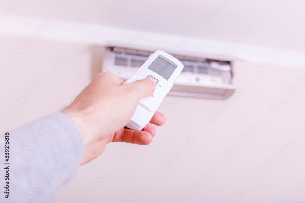 Close-up Of Young man hand operating air conditioner with remote control. Hand with remote control directed on the conditioner. Close-up Of Young man hand operating air conditioner with remote control. Hand with remote control directed on the conditioner.