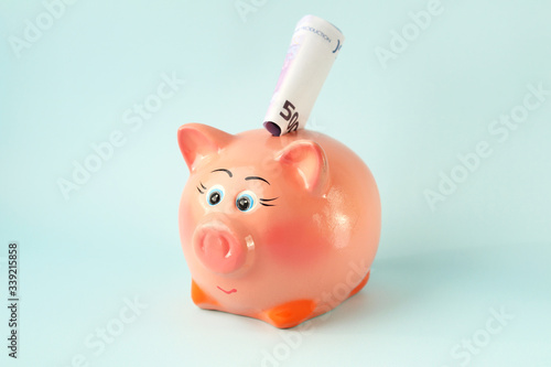 Pink piggy Bank with a rolled-up 500 Euro bill on a blue background. The monetary savings. Capital. Selective focus.