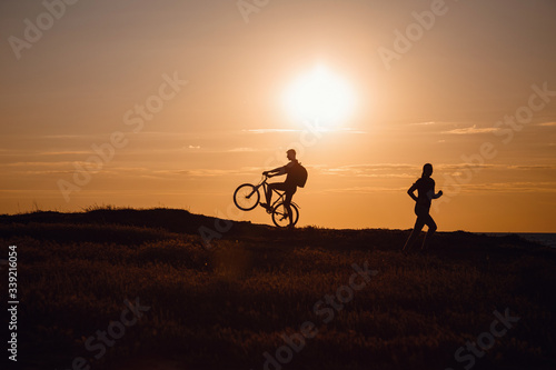 silhouette of men on a bicycle and a woman running towards him against a sunset