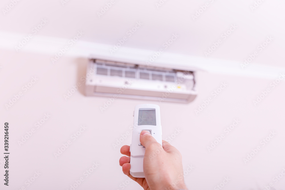 Air conditioner blowing warm air. Hand with remote control directed on the conditioner. Air conditioner blowing warm air. Hand with remote control directed on the conditioner.