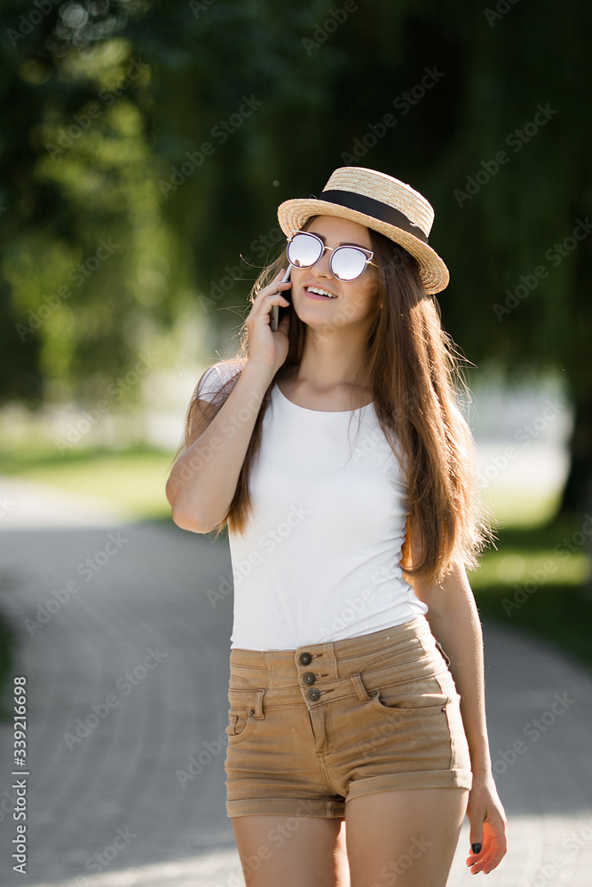 Young pretty woman using phone and walking in summer park.