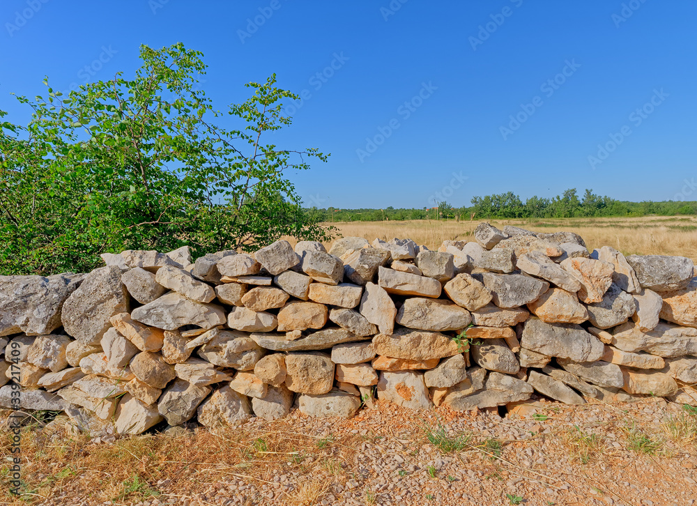 A dirt road in the heart of Dalmatia, bordered by a traditional stone fence, in Promina county in Croatia. Drywall construction is a protected intangible cultural heritage of humanity by UNESCO. A dirt road in the heart of Dalmatia, bordered by a traditional stone fence, in Promina county in Croatia. Drywall construction is a protected intangible cultural heritage of humanity by UNESCO.
