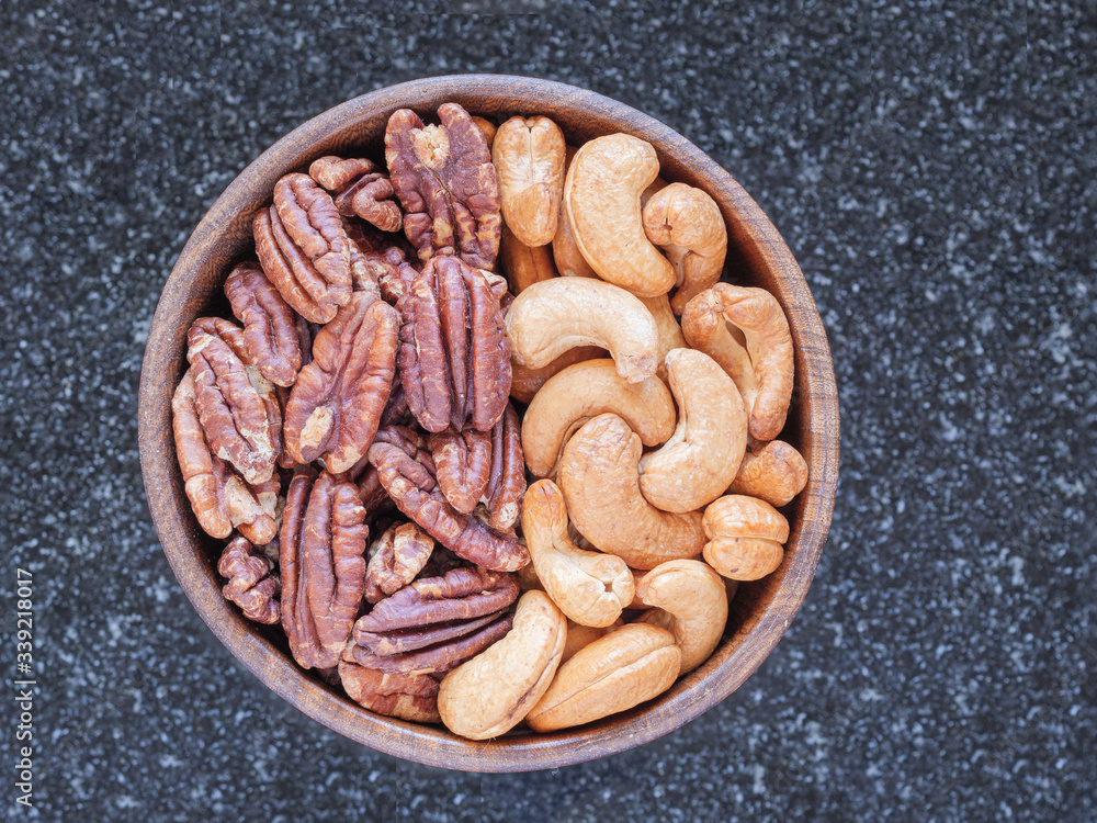 Fototapeta premium View from above of a bowl of roasted unsalted cashew and pecans in a wooden bowl on a marble kitchen table. 