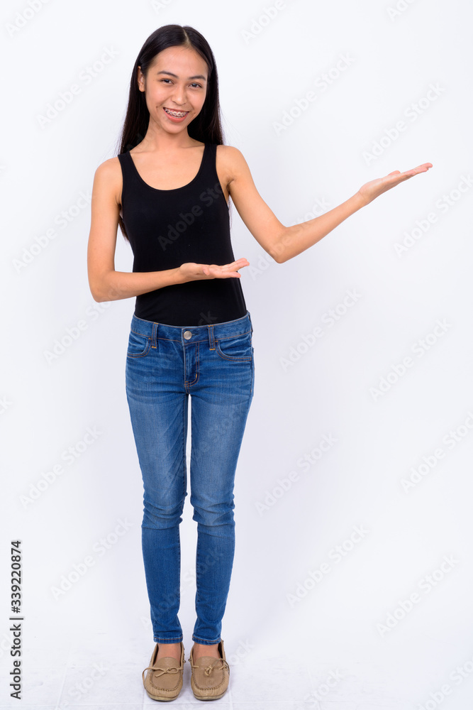Full body shot of happy young beautiful Asian woman showing something Full body shot of happy young beautiful Asian woman showing something