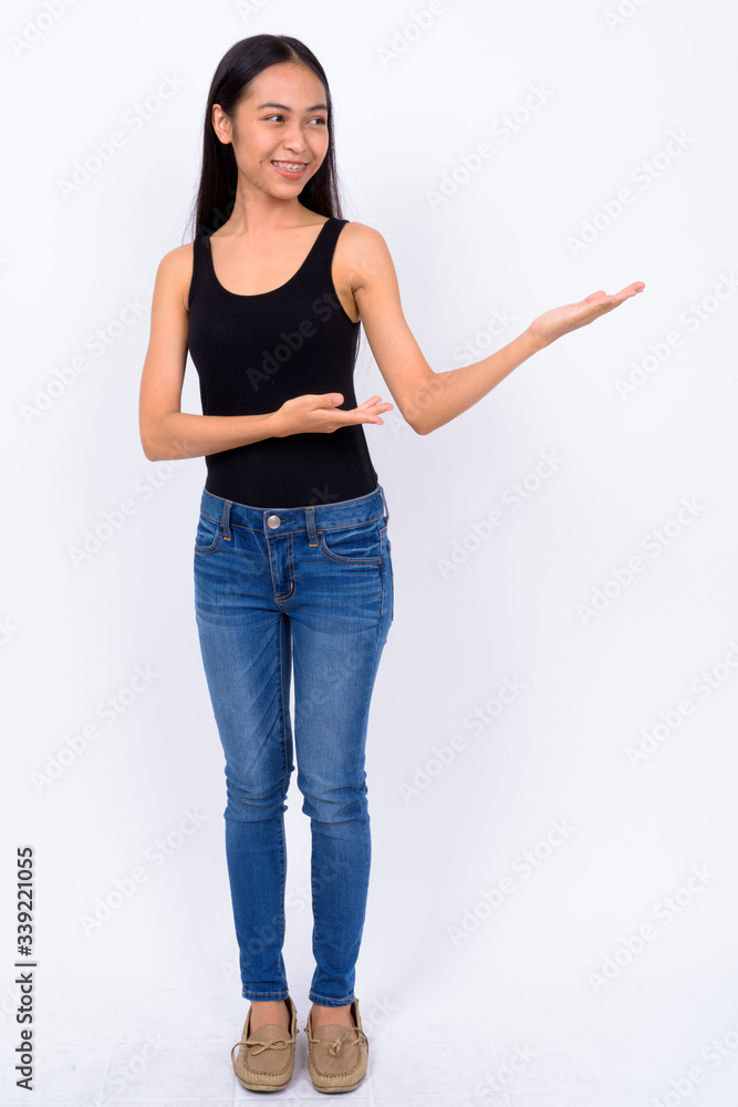 Full body shot of happy young beautiful Asian woman showing something Full body shot of happy young beautiful Asian woman showing something