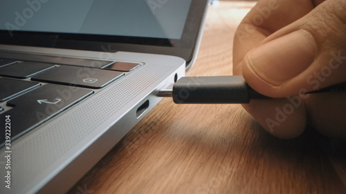 Close-up Macro Shot: Laptop on the Desk, Person Inserts USB-C Cable Adapter into Computer Port.  photo