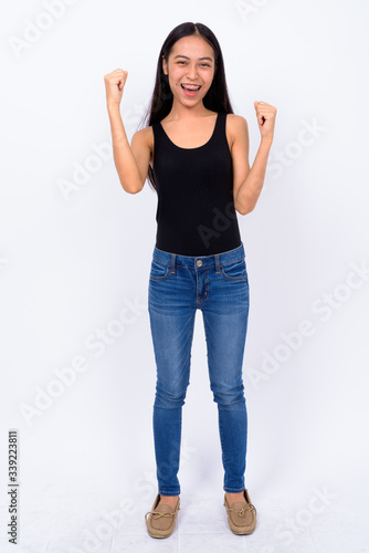 Full body shot of happy young Asian woman with fists raised