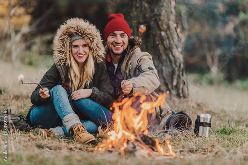 Traveler couple camping and roasting marshmallows over the fire in the forest after a hard day. Concept of trekking, adventure and seasonal vacation.