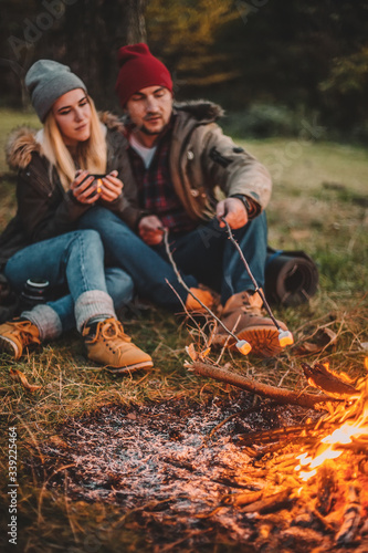 Traveler couple camping and roasting marshmallows over the fire in the forest after a hard day. Concept of trekking  adventure and seasonal vacation.