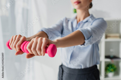 cropped view of businesswoman training with pink dumbbells in office, selective focus