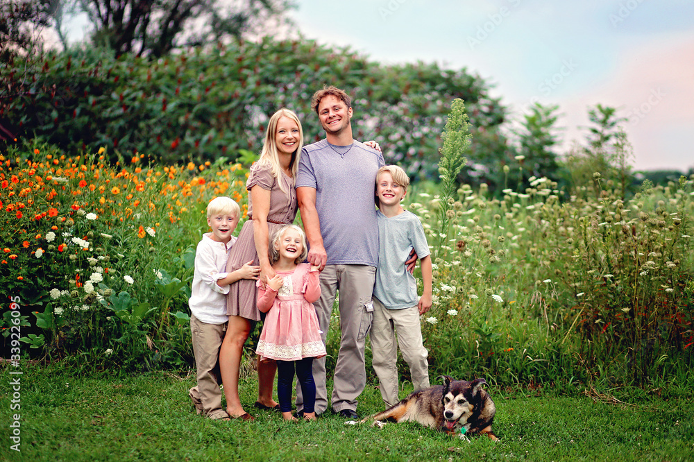 Happy Wholesome Caucasian Family and Dog Smiling and Posing by Flowers