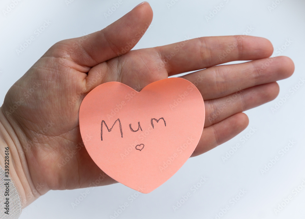 Obraz premium Woman's hand holding pink heart-shaped sticky note with hand written word 