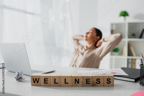 selective focus of businesswoman relaxing at workplace with laptop and alphabet cubes with wellness word