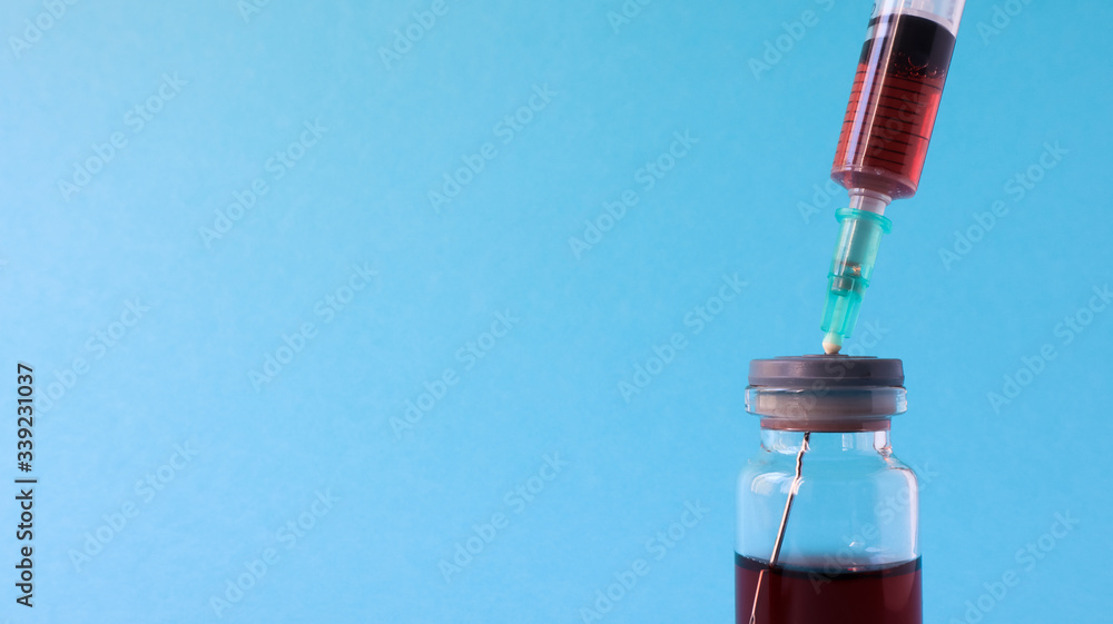A syringe sticks out of a red liquid bottle. Isolated on a blue background. Medicine, injections, vaccines and disposable syringes, drug concept. Sterile bottle. Glass ampoule medical for injection. A syringe sticks out of a red liquid bottle. Isolated on a blue background. Medicine, injections, vaccines and disposable syringes, drug concept. Sterile bottle. Glass ampoule medical for injection.