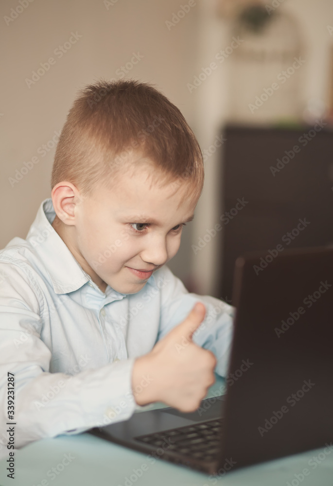 Boy sitting on the table and talking online. Workspace office desk with laptop. Kid learning online. Distance learning online education.