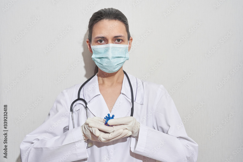 A young woman doctor in a disposable medical mask, standing and holding a blue virus, a global disease pandemic outbreak A young woman doctor in a disposable medical mask, standing and holding a blue virus, a global disease pandemic outbreak