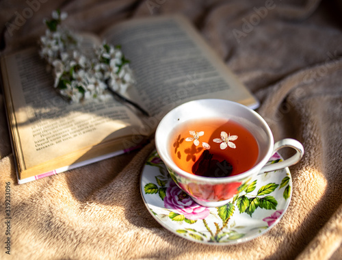 mug of tea, black tea in a mug, a sprig of blossoming, a shadow, on a plaid stands a mug of tea,