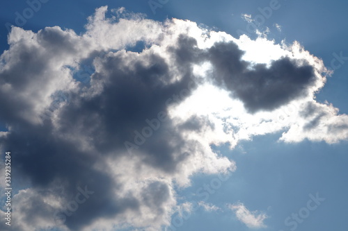 White light fluffy clouds in a blue sky with a solar flare.