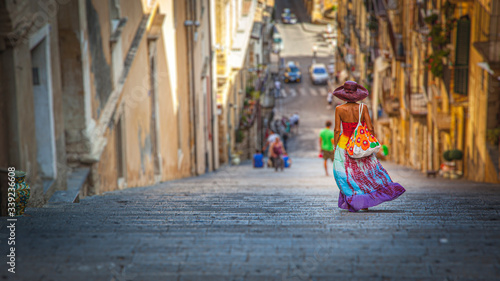 Tanned young woman, with multicolored dress and hat, goes down the staircase of Caltagirone in Sicily