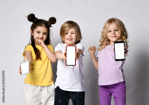 Portrait of three smiling children kids in casual clothes showing us blank screens of their smartphones