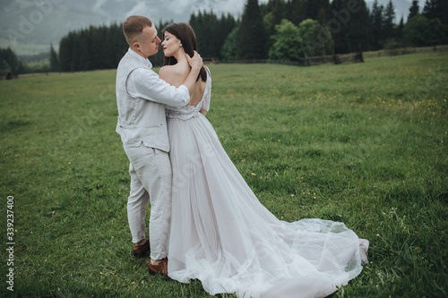 Spring wedding in the mountains. A guy in a shirt and vest and a girl in a white dress hug and kiss on a background of mountains and a forest