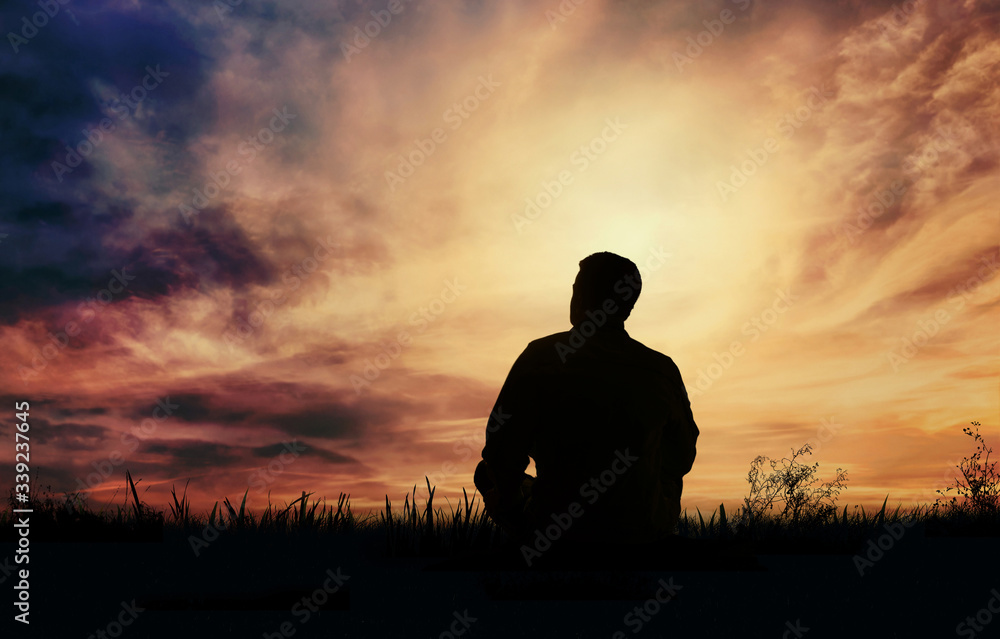Silhouette of a man sitting in a meadow at sunset