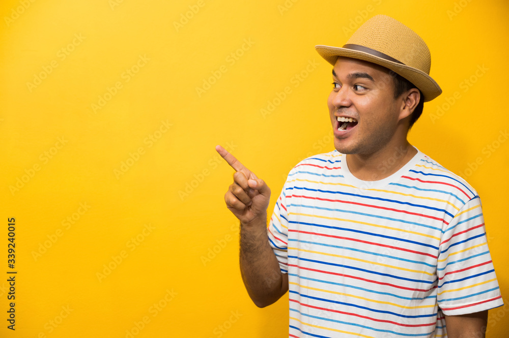 Young happy&funny asian man pointing finger on blank space for text on yellow background.