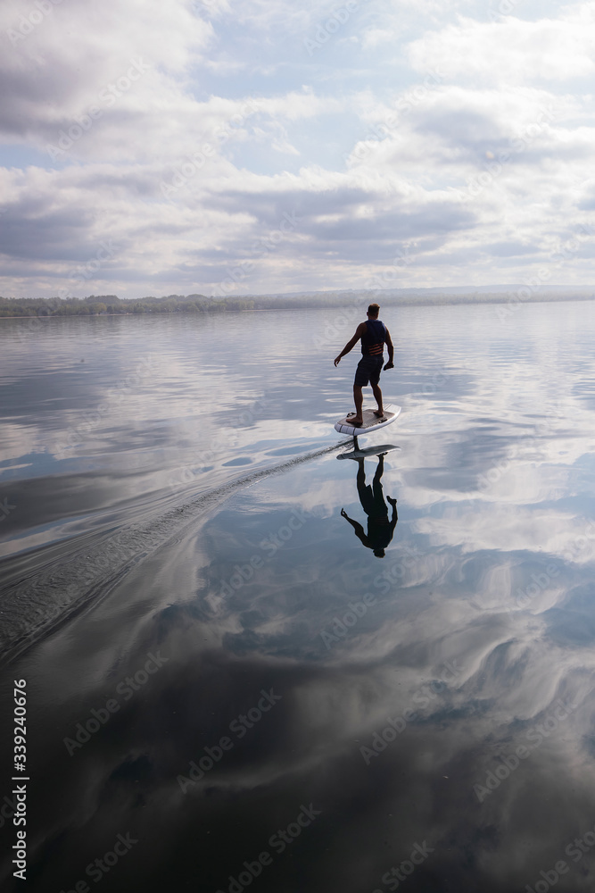 Man riding an electric hydrofoil foil board on a lake with a life jacket