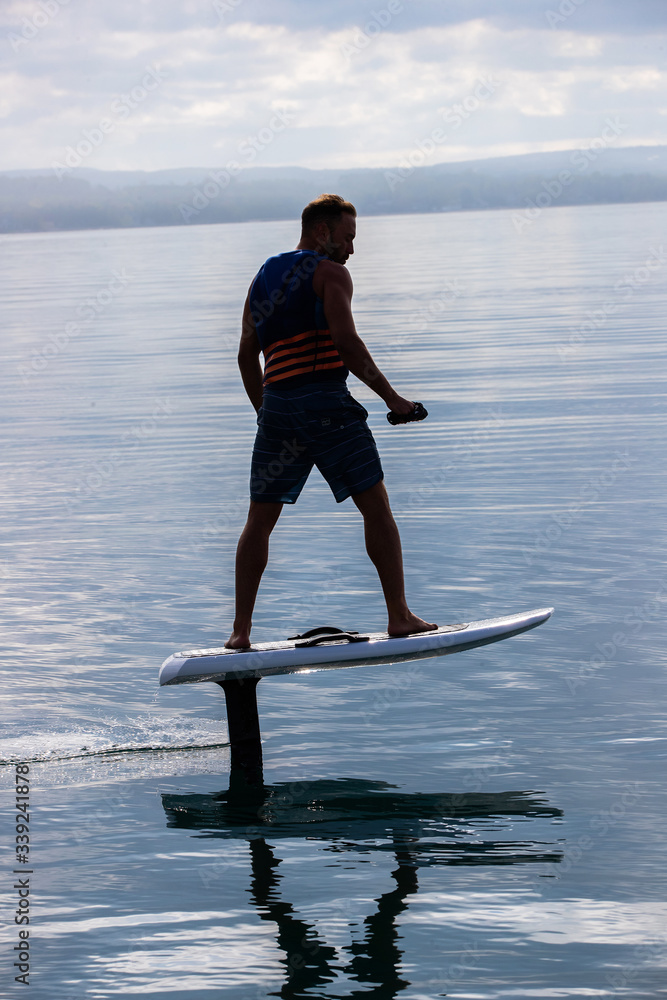 Man riding an electric hydrofoil foil board on a lake with a life jacket