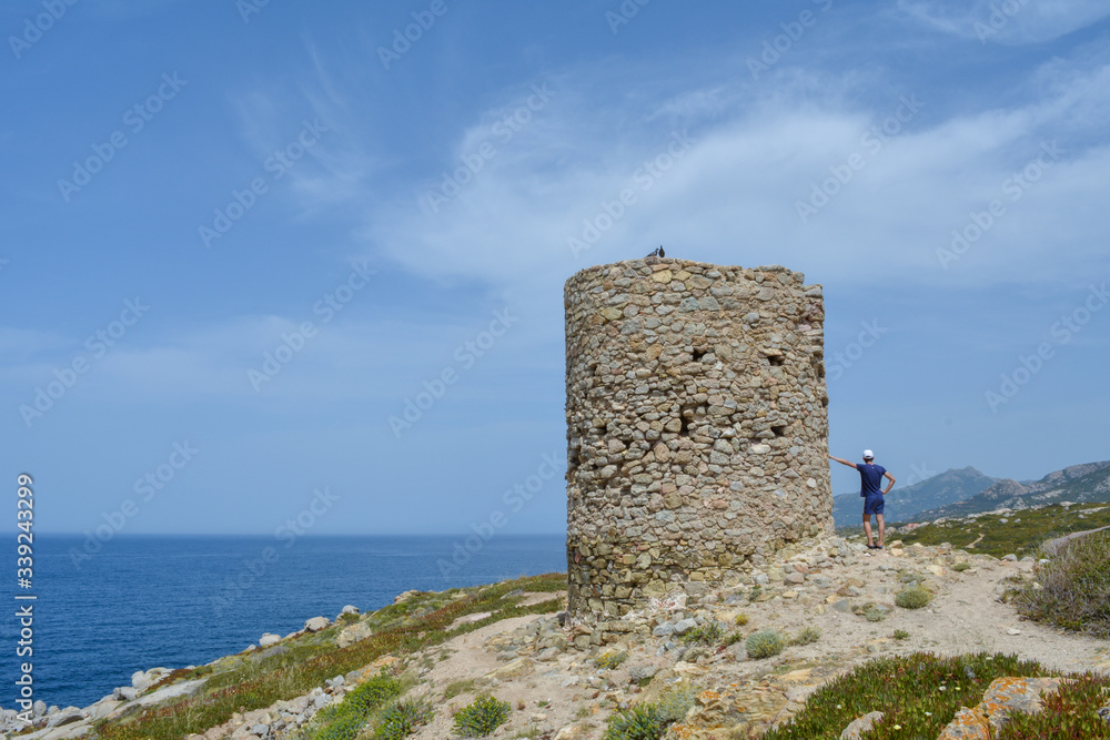 Young man near the genoese tower at Punta Spano amongst the maquis and rocks, Balagne region of Corsica, France