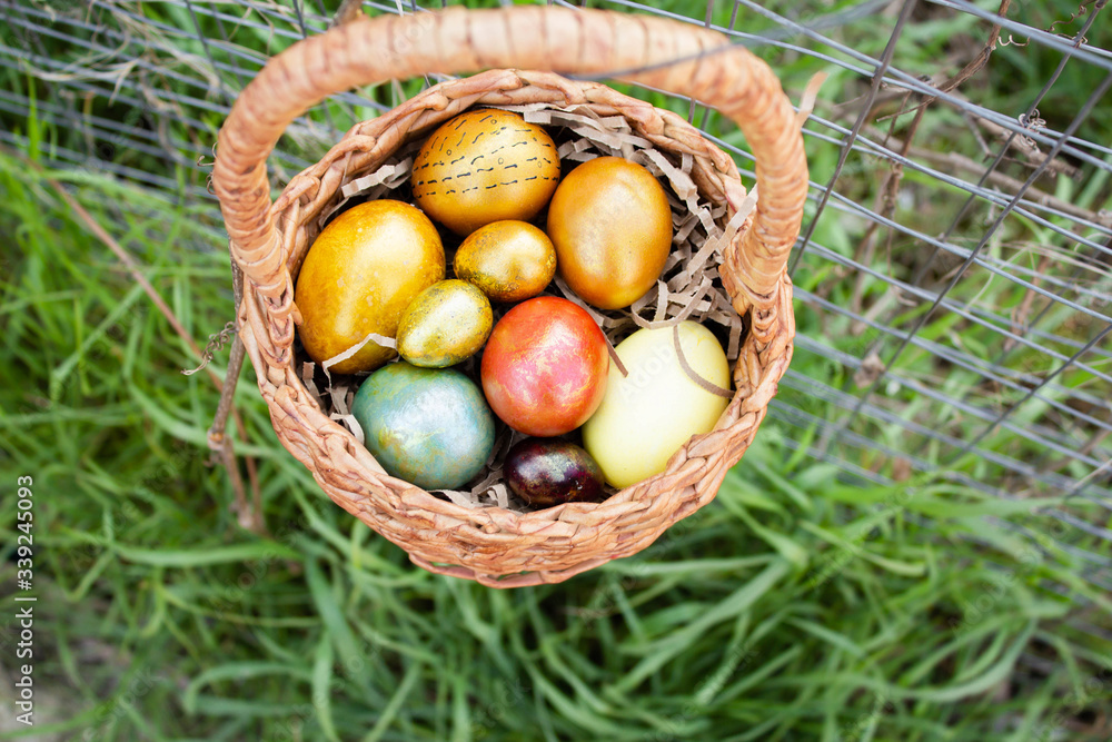 A basket of Easter eggs hangs on the fence against the background of green grass. A basket of Easter eggs hangs on the fence against the background of green grass.