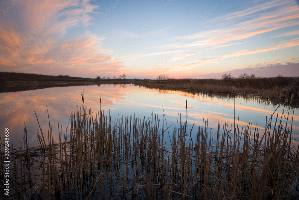 Reflections of a vivid sunset sky streak across the surface of a wetland marsh northern Illinois.
