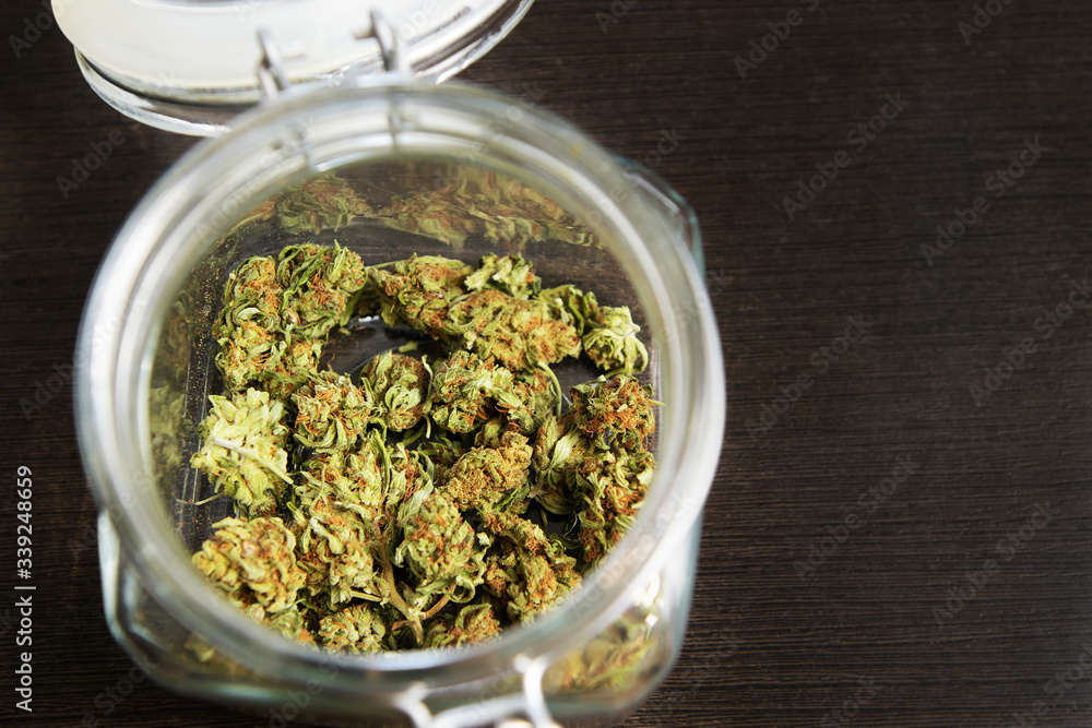 Cannabis buds in glass jar closeup on wooden background. Cannabis buds in glass jar closeup on wooden background.
