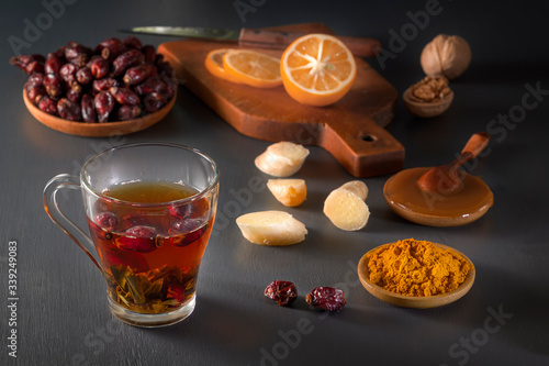 Medicinal herbal tea in a glass cup, ginger, walnut, turmeric, honey, lemon and dry rosehip berries - a means to increase immunity from the virus