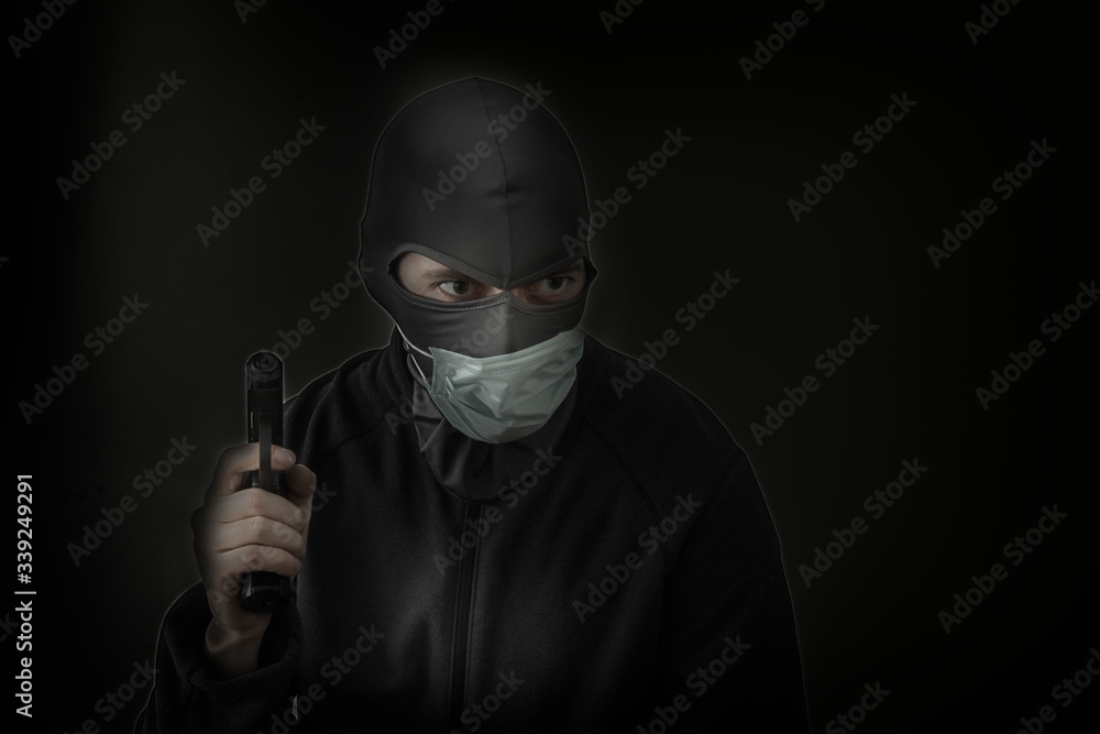 Bandit in a black mask with a slot for the eyes and a medical mask with a gun in his hands. Low hatch. Close-up. Copy space Bandit in a black mask with a slot for the eyes and a medical mask with a gun in his hands. Low hatch. Close-up. Copy space
