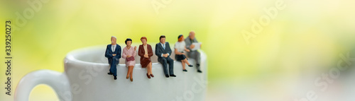 Miniature people: Business team sitting on cup of coffee with copy space using as background business cover page concept.
