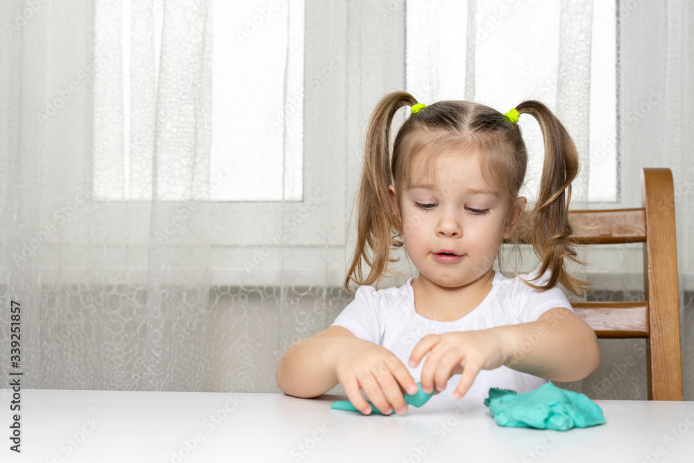 girl preschooler sits at a table and sculpts from turquoise dough for tepka. activities with children at home on self-isolation in connection with coronavirus infection girl preschooler sits at a table and sculpts from turquoise dough for tepka. activities with children at home on self-isolation in connection with coronavirus infection