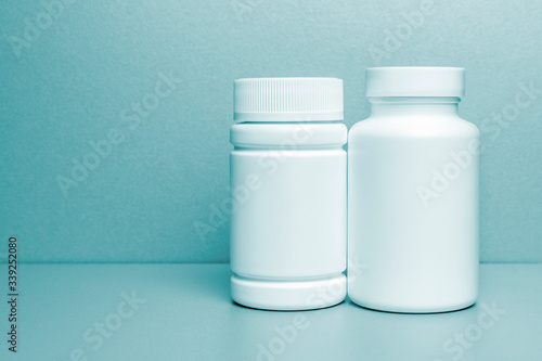 2 white jars for medicines and vitamins and dietary supplements without a name are on a gray shelf. copy space to the left. layout for a pharmacy, a store. blue tinted