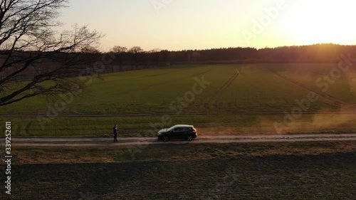 Schwarzes Auto SUV auf Feldweg voller Staub beim Sonnenuntergang fährt auf Person zu während der Corona Pandemie