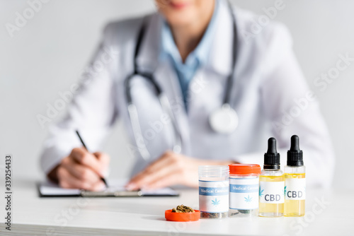 selective focus of dried marijuana, bottles with cbd and medical cannabis lettering near doctor writing prescription