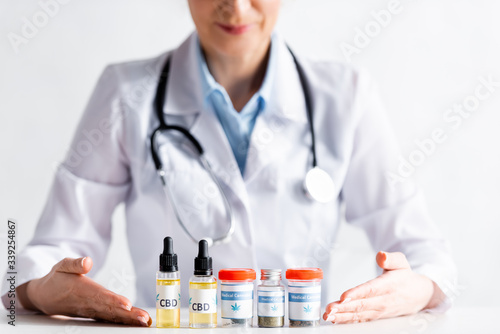 cropped view of doctor pointing with hands at bottles with medical cannabis and cbd lettering