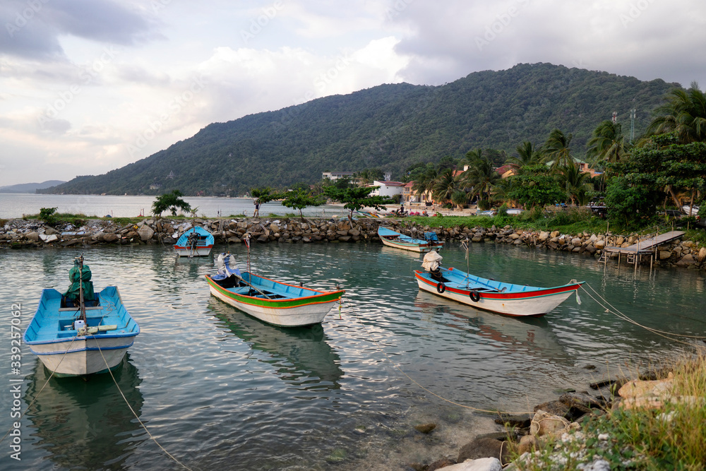Traditional fishing boats at the pier of Koh Phangan island in Thailand at sunset on a cloudy day.