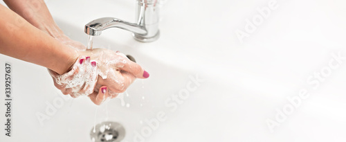 Young woman washing her hands under water tap faucet with soap, nails covered purple polish. Wide banner space for text right side. Personal hygiene concept - coronavirus covid-19 outbreak prevention