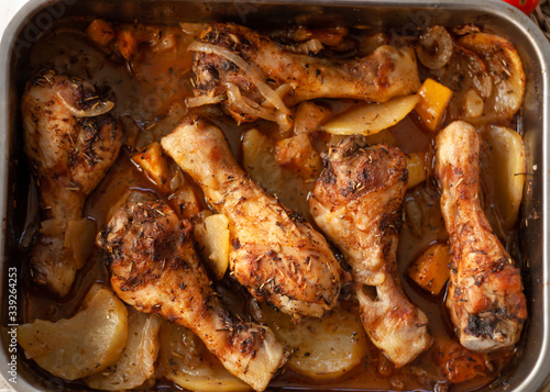 Roasted Chicken legs on metal baking tray with potatoes, onion. tomatoes witn spices. Top view. © Larusset