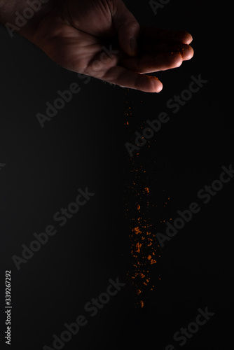 A man's hand scattering and tossing up a nice and fresh red paprika on black background with strong light. Paprika is nice seasoning with pretty colour